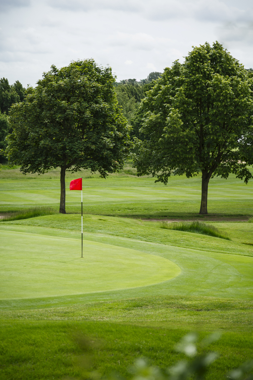 Red flag on a golf course with trees in England, UK