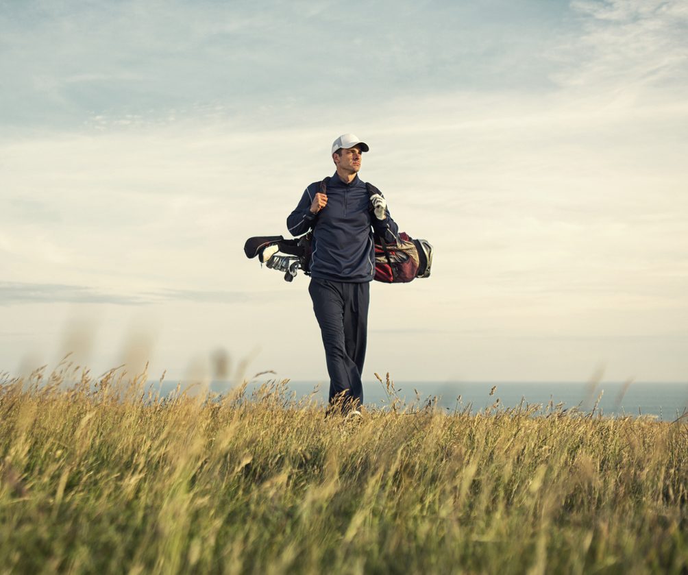 A male adult golfer walks to the green atop a links golf course in North Devon, England.